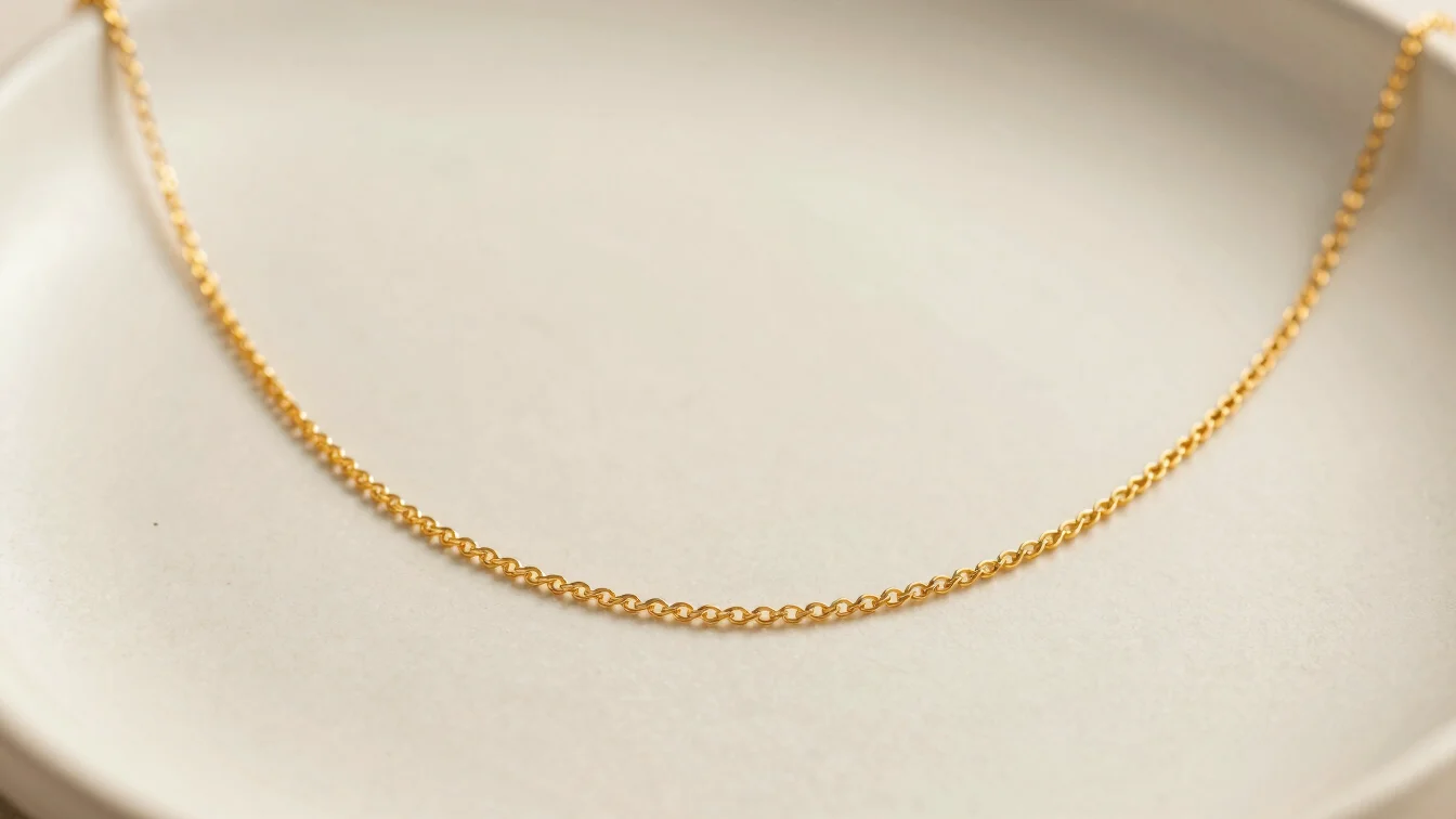 Close-up shot of a fine gold chain necklace resting on ceramic texture, warm lighting