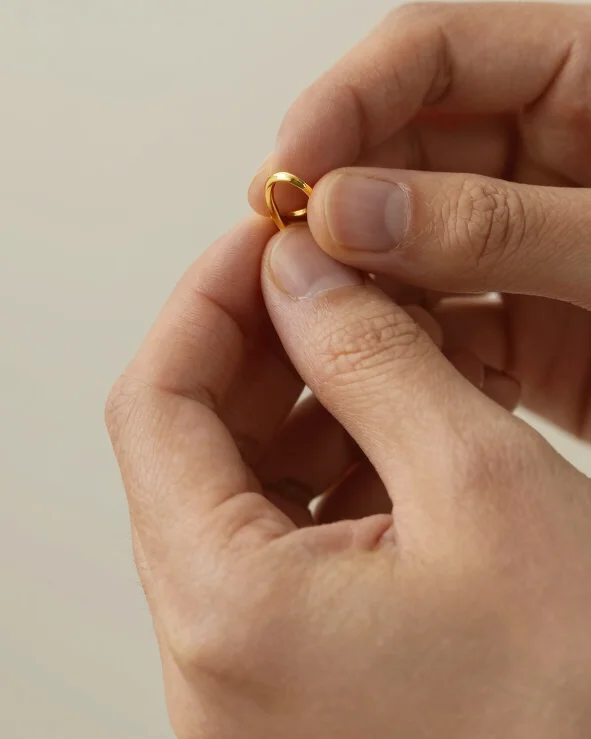 Portrait close-up shot of hand polishing a gold piece on bench, soft studio light, neutral background